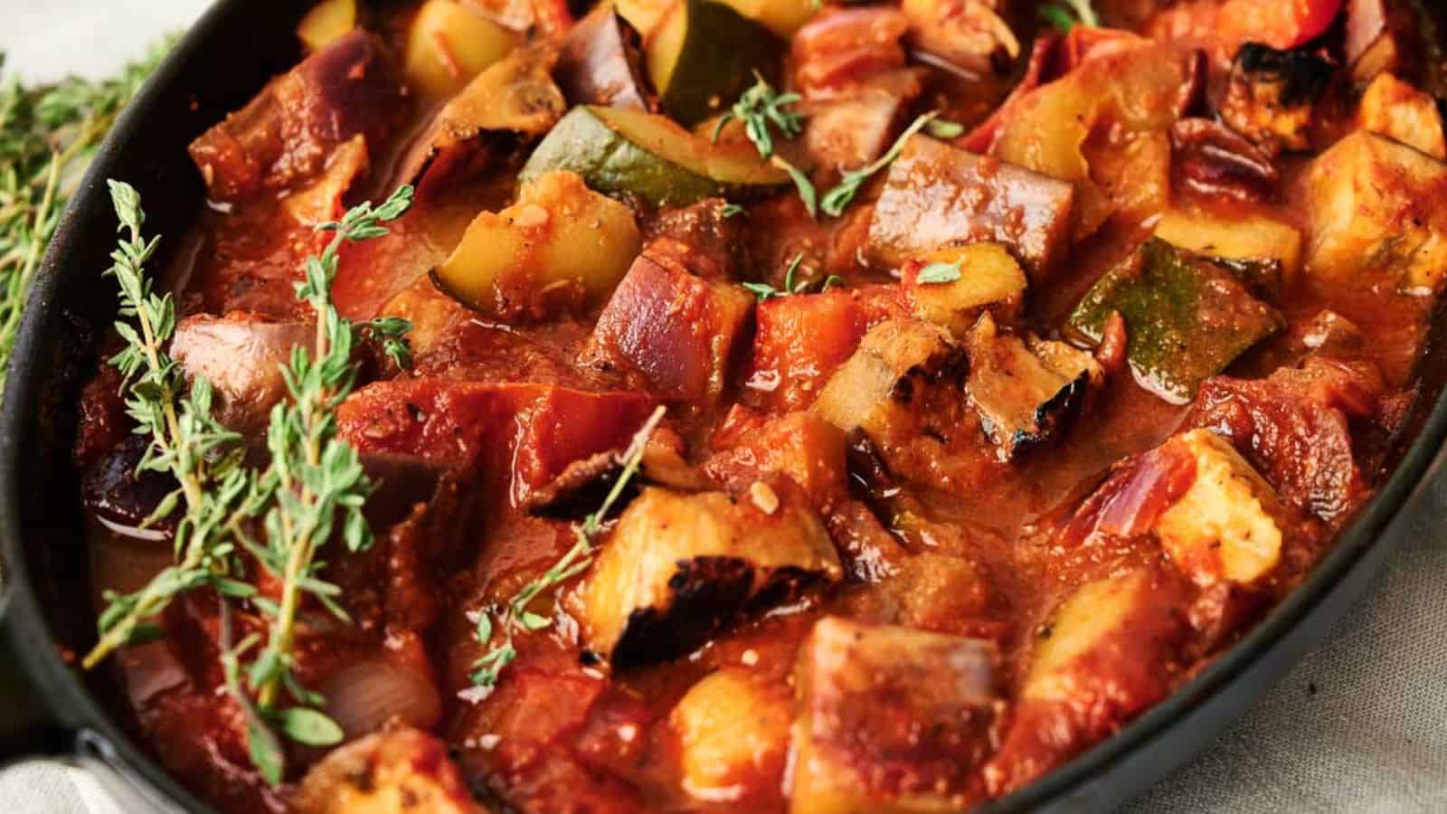 A colorful plate of ratatouille with layers of zucchini, eggplant, and tomatoes cooked in a savory sauce, garnished with fresh herbs.