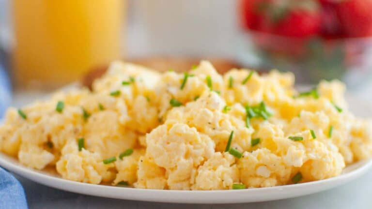 A close-up of scrambled eggs mixed with cream cheese and garnished with fresh herbs.