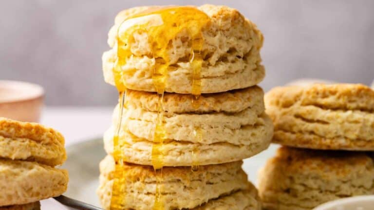 A stack of flaky, golden-brown sourdough biscuits drizzled with honey, showcasing their airy and soft interior.