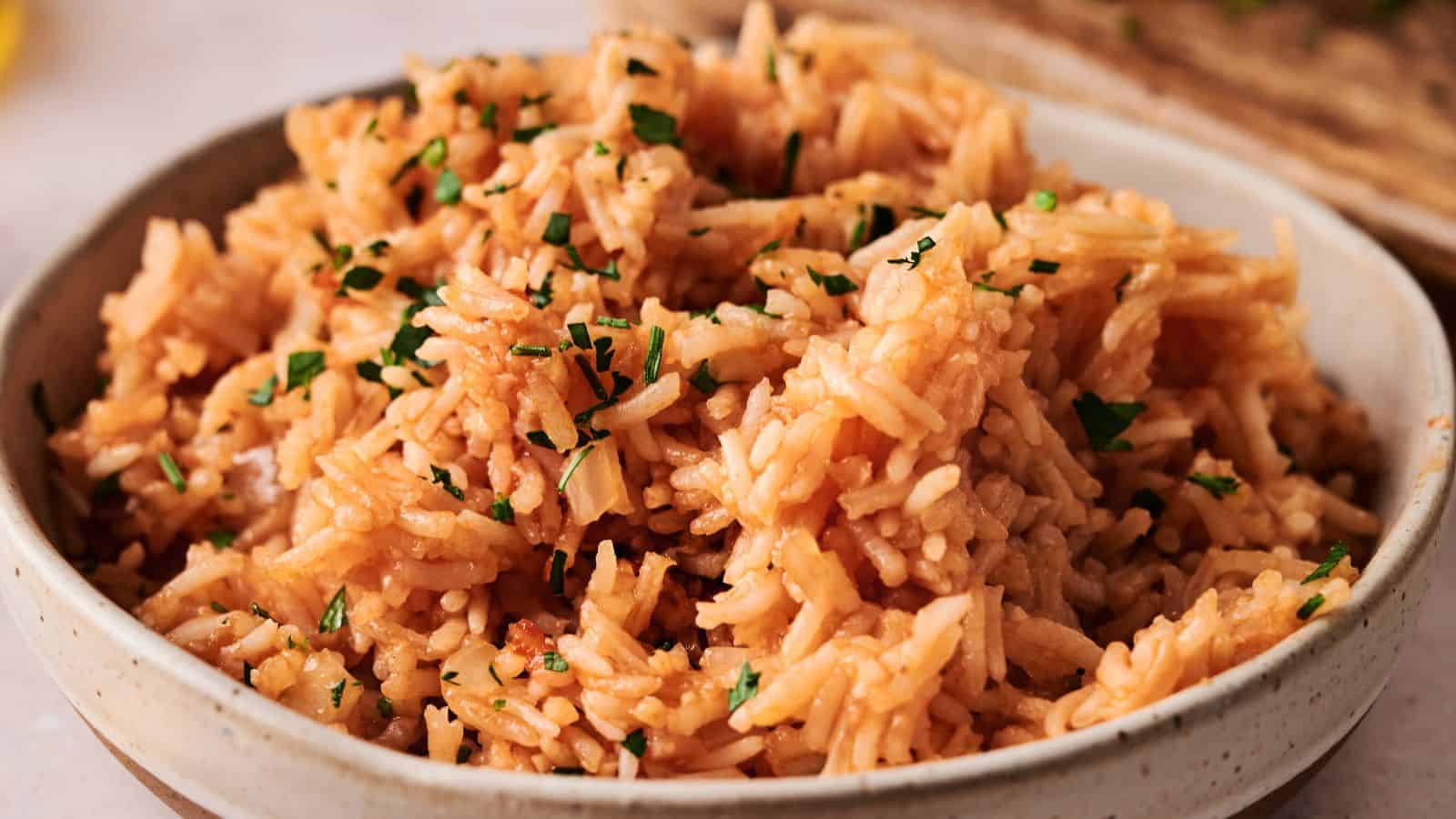 A bowl of seasoned rice garnished with chopped herbs, served in a beige ceramic dish.