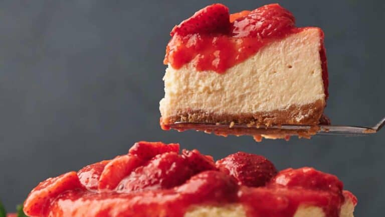 A slice of strawberry cheesecake with a rich graham cracker crust, topped with fresh strawberry sauce and whole strawberries.