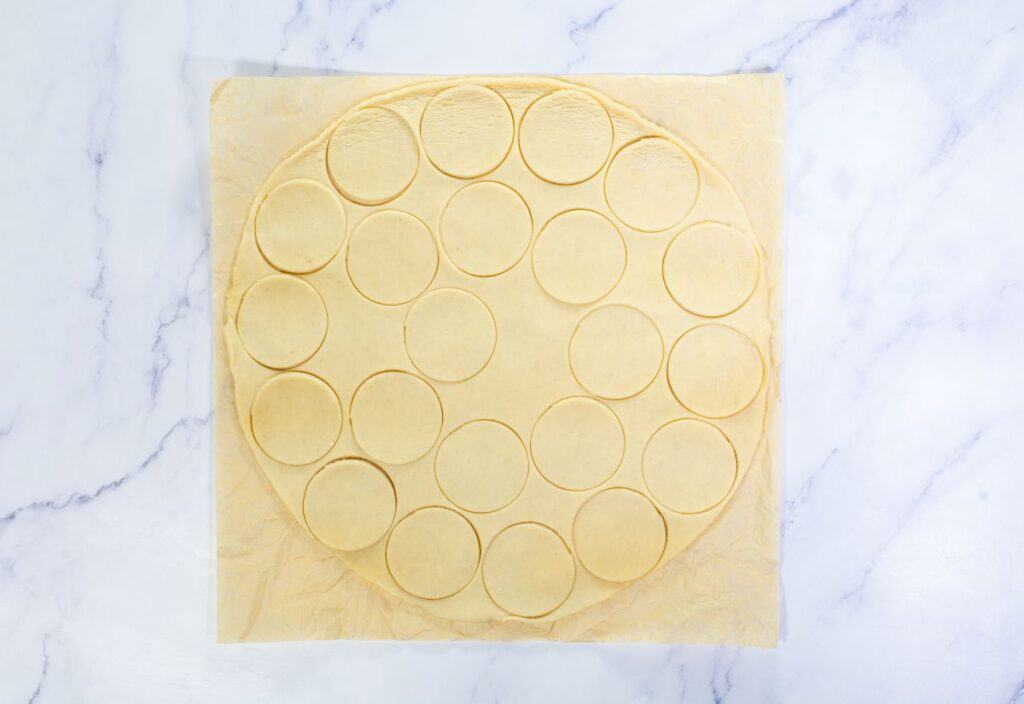 A circle of pie dough with cut-out circles for mini tartlet shells before baking.