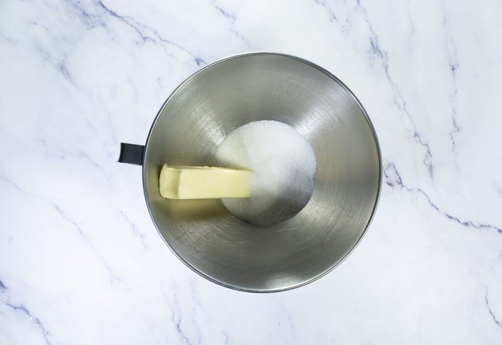 A close-up of unsalted butter and sugar in a mixing bowl, ready to be creamed together to start the cookie dough.
