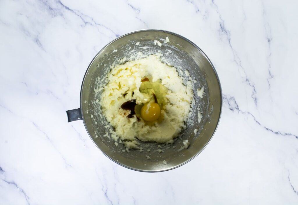 A mixing bowl with butter, sugar, egg, and vanilla extract combined, showing a creamy mixture in preparation for the dough.