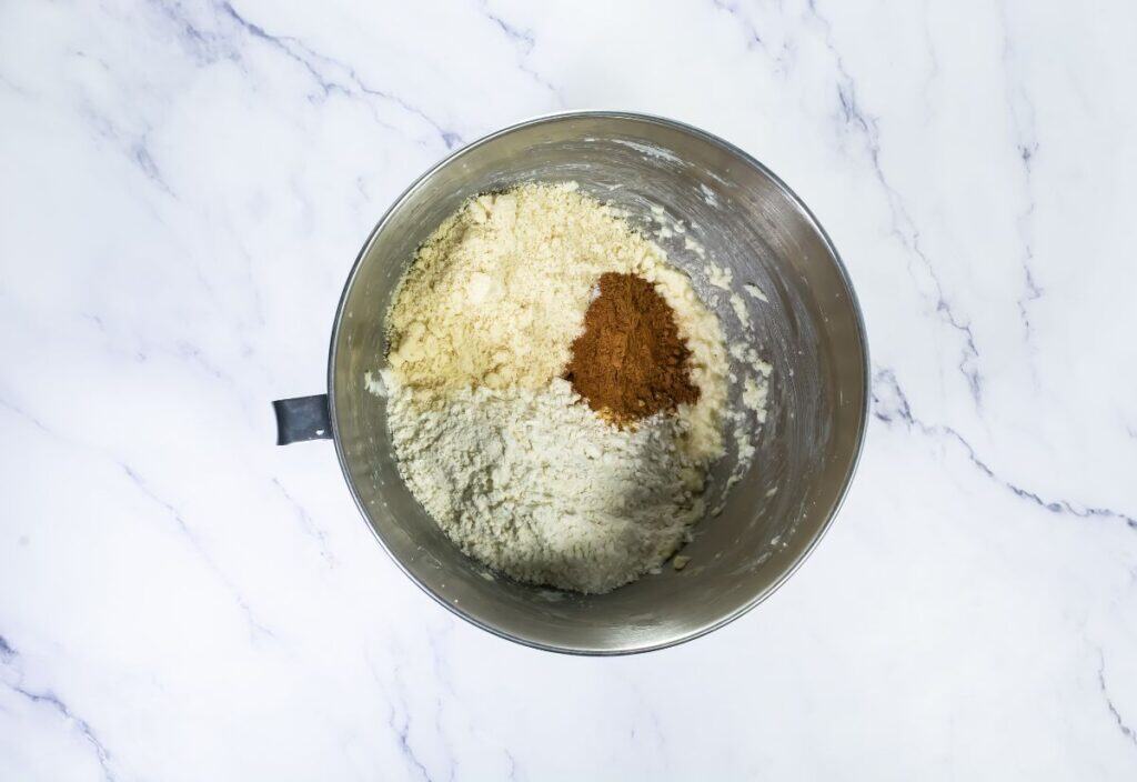 The dry ingredients, including almond flour, flour, and spices like cinnamon, placed in the mixing bowl to be incorporated into the dough.