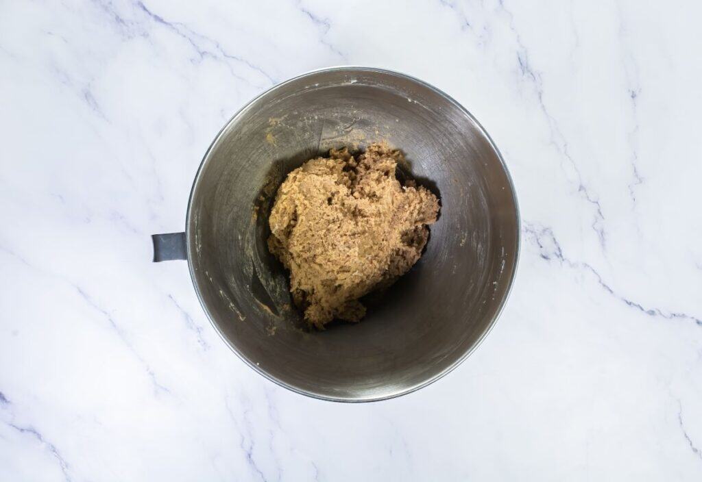 The cookie dough formed after mixing all ingredients, showing a thick, slightly crumbly texture in the mixing bowl.
