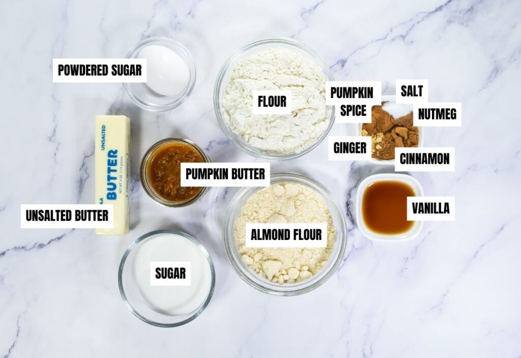 A collection of ingredients for Pumpkin Linzer Cookies laid out in bowls, including unsalted butter, sugar, pumpkin butter, almond flour, and various spices like cinnamon, nutmeg, and ginger.
