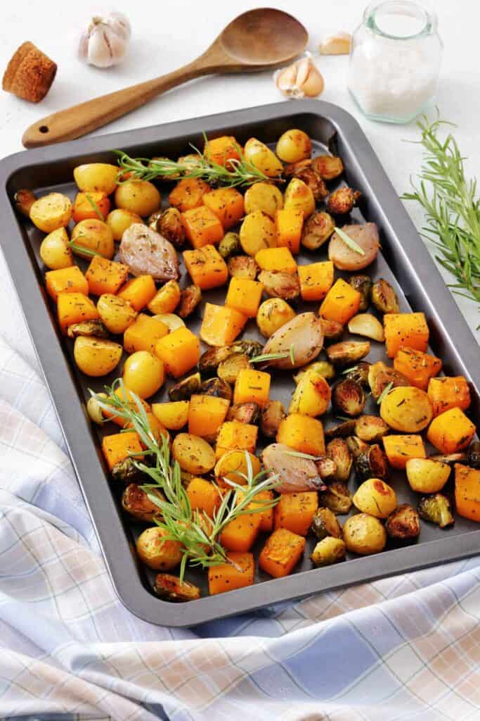 Sheet pan filled with roasted butternut squash, Brussels sprouts, baby potatoes, garlic, and shallots topped with rosemary.