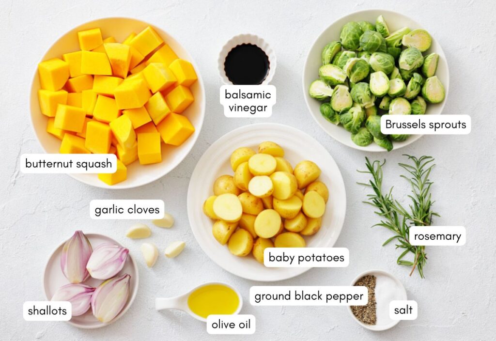 Flat lay of recipe ingredients including bowls of butternut squash, Brussels sprouts, baby potatoes, garlic, shallots, olive oil, balsamic vinegar, rosemary, salt, and pepper.