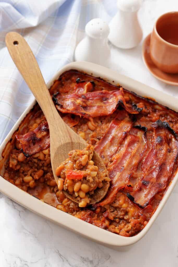 A serving of Southern Ground Beef & Baked Bean Casserole on a plate with a fork, topped with crispy bacon.