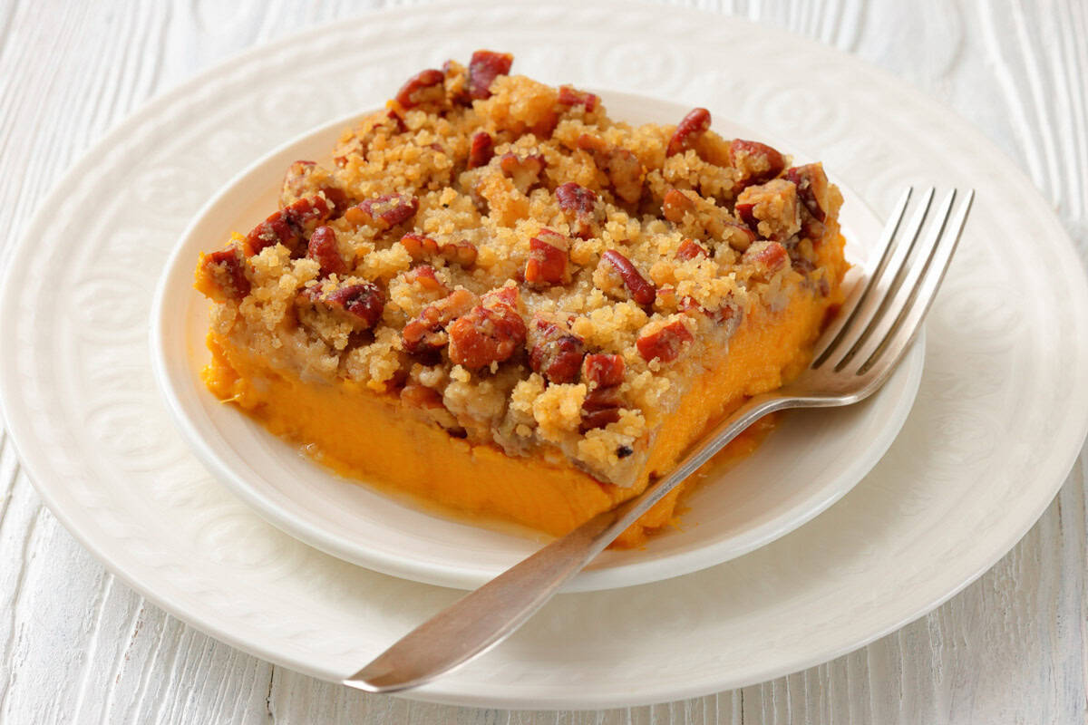 A serving of sweet potato casserole with a golden pecan streusel topping on a plate, with a fork on the side.