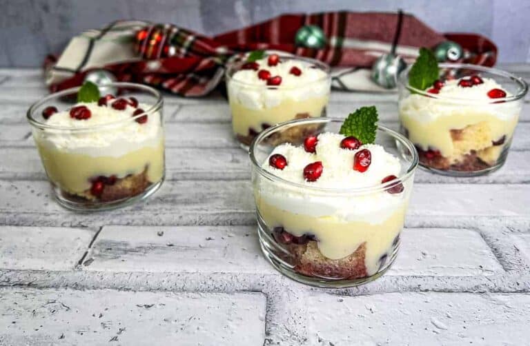 Glass cups filled with layers of trifle, featuring sponge cake, whipped cream, and pomegranate seeds.