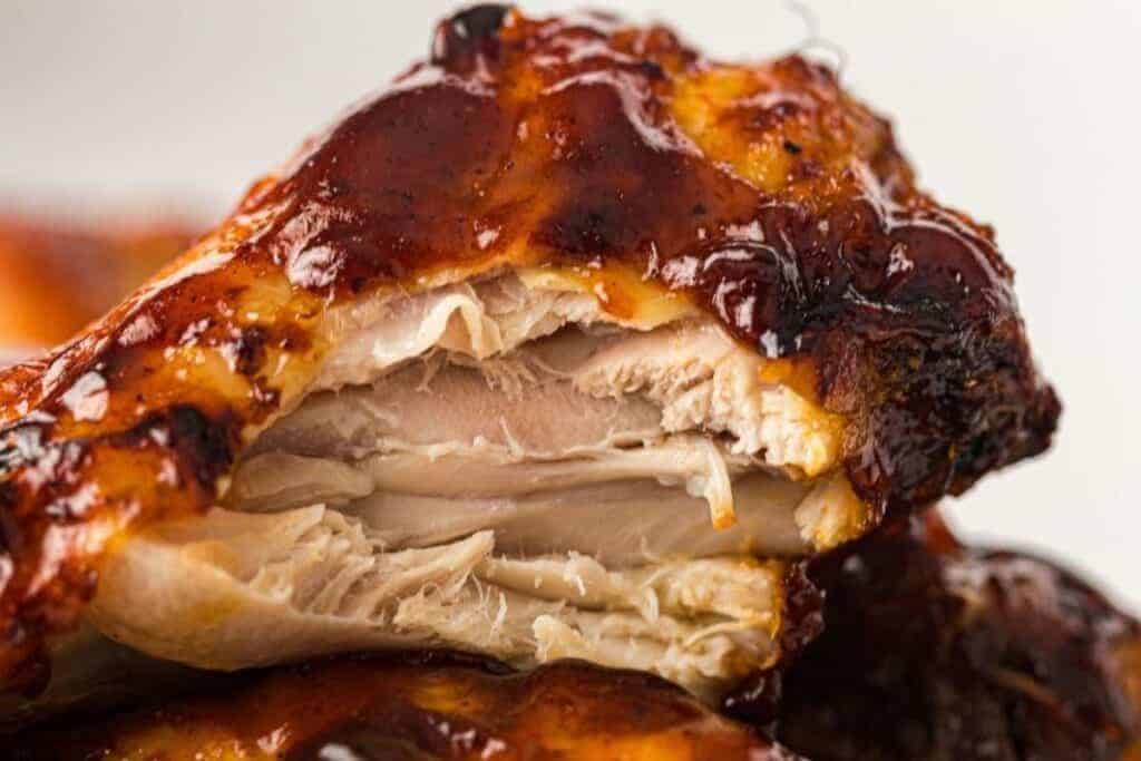 Close-up of a cooked chicken wing with a bite taken, showing juicy and tender meat covered in dark barbecue sauce.