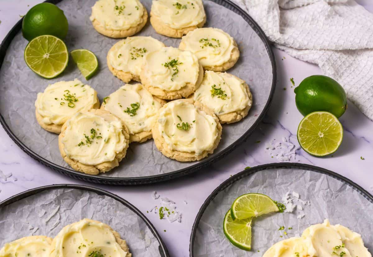 Llime-flavored cookies with cream and lime zest, arranged on a tray with lime slices on the side.
