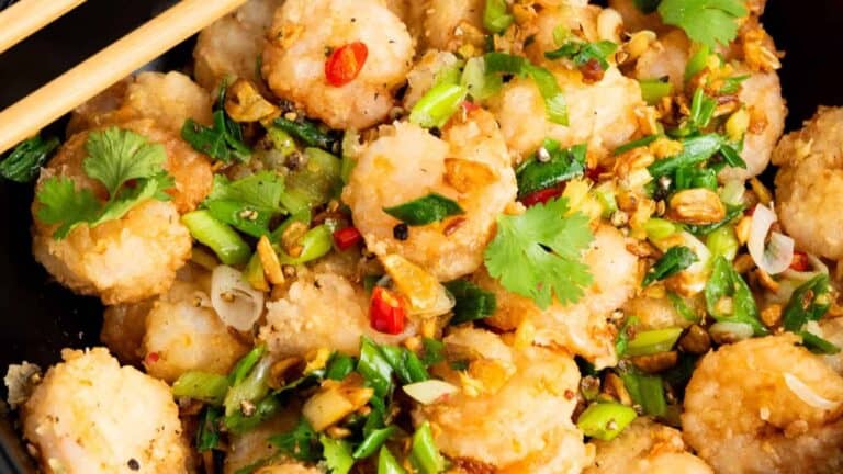 A close-up of shrimp stir-fried with green onions, cilantro, and red chili pepper, garnished with crushed garlic and green onions.
