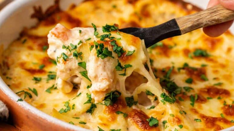 A creamy crab dip, topped with melted cheese and garnished with fresh herbs, served in a dish with a wooden spoon.