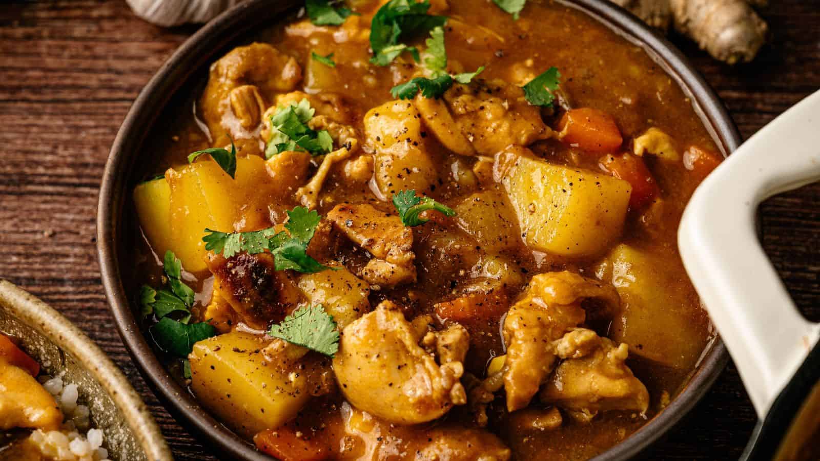 A bowl of chicken stew with chunks of potato and carrot, garnished with chopped cilantro, on a wooden surface.