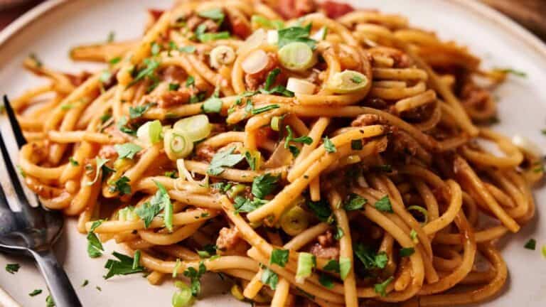 A close-up of Mexican spaghetti garnished with green onions and parsley, showcasing the hearty, flavorful noodles and sauce.