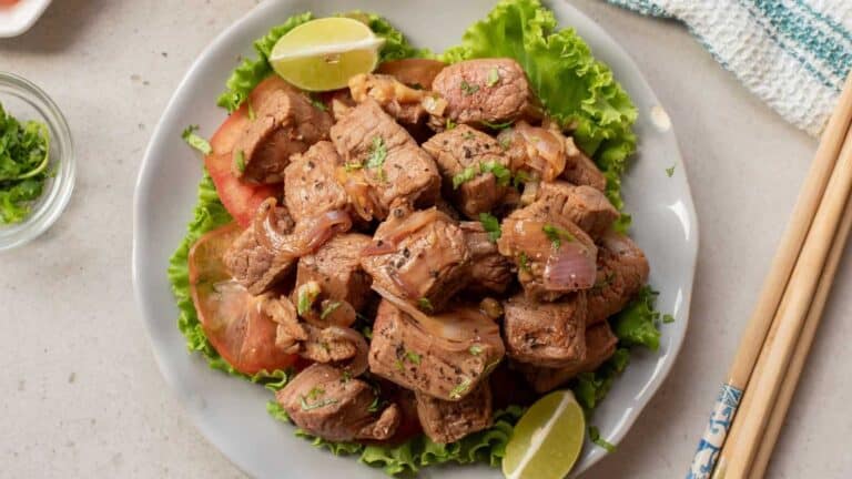 Vietnamese shaking beef with tender cubes of beef, stir-fried with vegetables and served with a side of rice and garnished with fresh herbs.