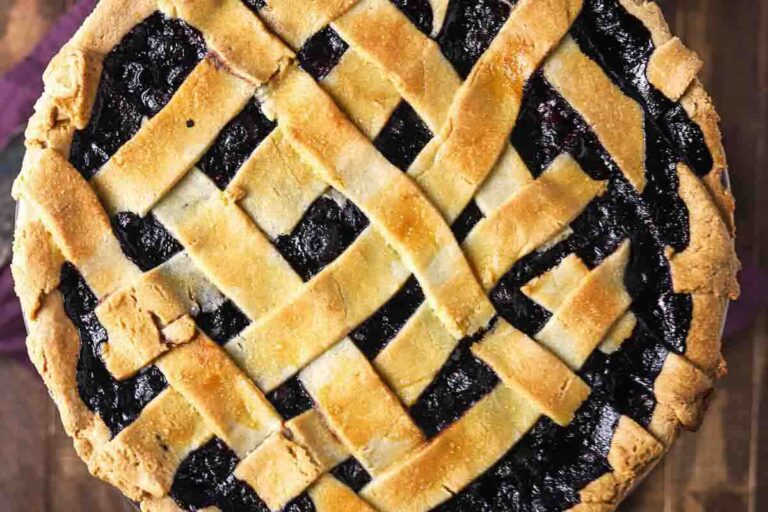 A close-up view of a baked pie with a golden-brown lattice crust and dark fruit filling.