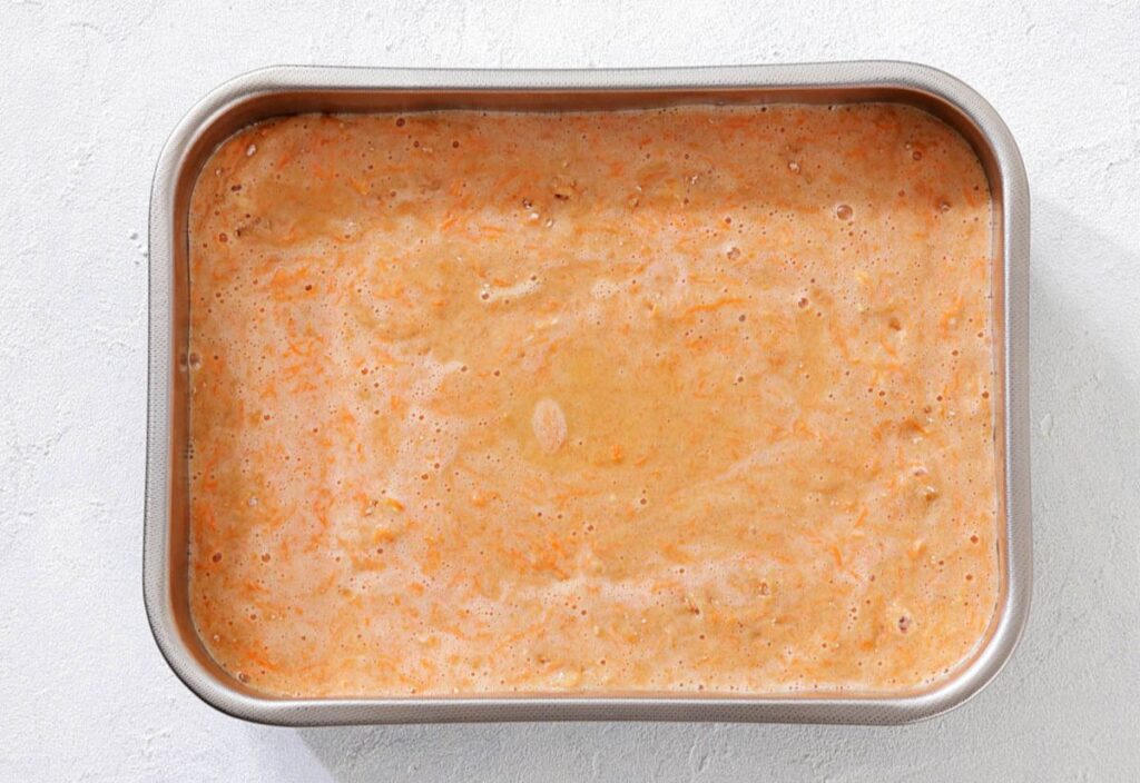Rectangular pan filled with uncooked carrot cake batter.