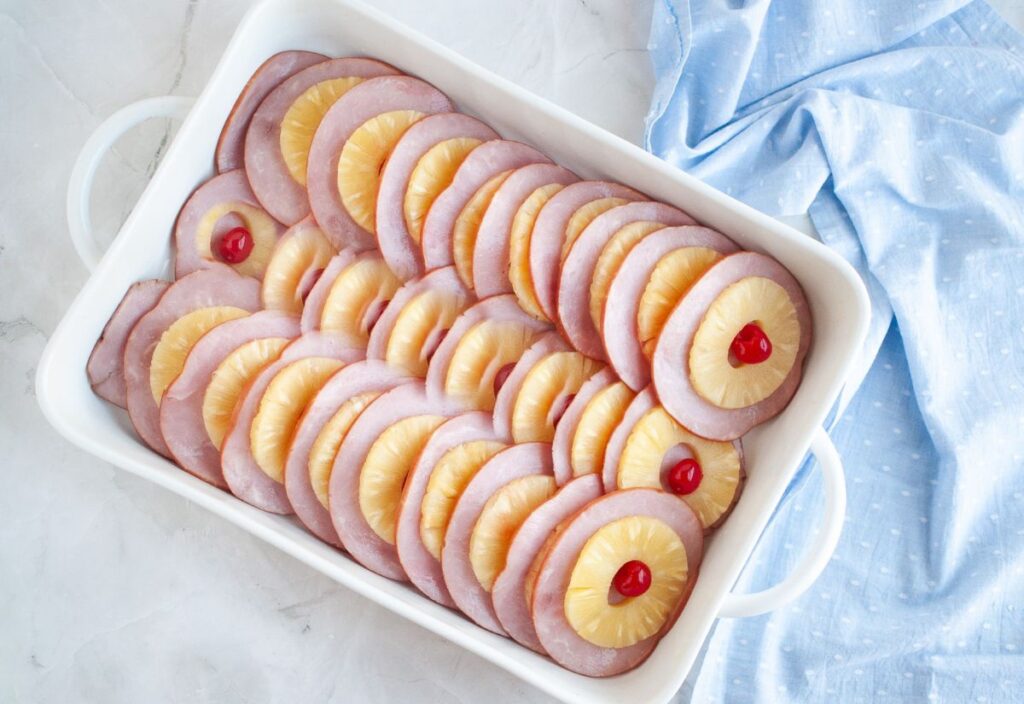 Baking dish with layered ham slices, pineapple rings, and cherries.