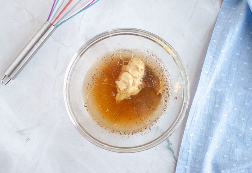 Glass bowl with pineapple juice, Dijon mustard, brown sugar, vinegar, melted butter, pepper, and cloves.