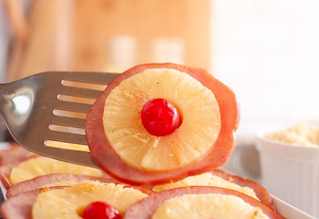 A closeup shot of a Glazed Ham Slice with pineapple ring and cherry.