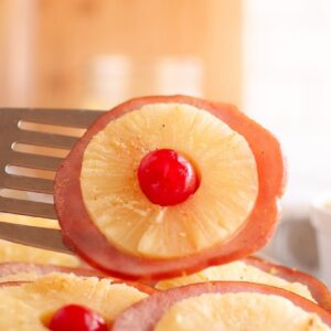 A closeup shot of a Glazed Ham Slice with pineapple ring and cherry.