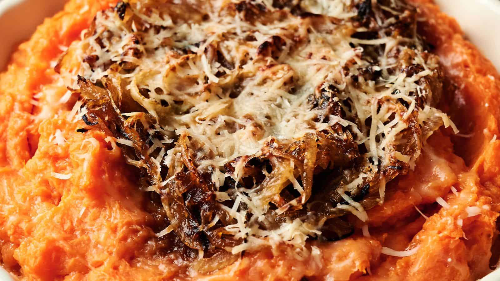 Mashed sweet potatoes topped with caramelized onions and grated cheese in a white dish.