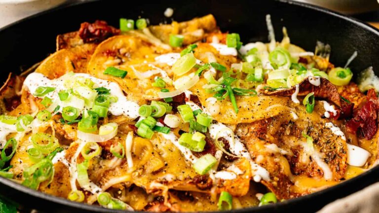 A skillet filled with loaded nachos, topped with melted cheese, sour cream, chopped green onions, and various seasonings.