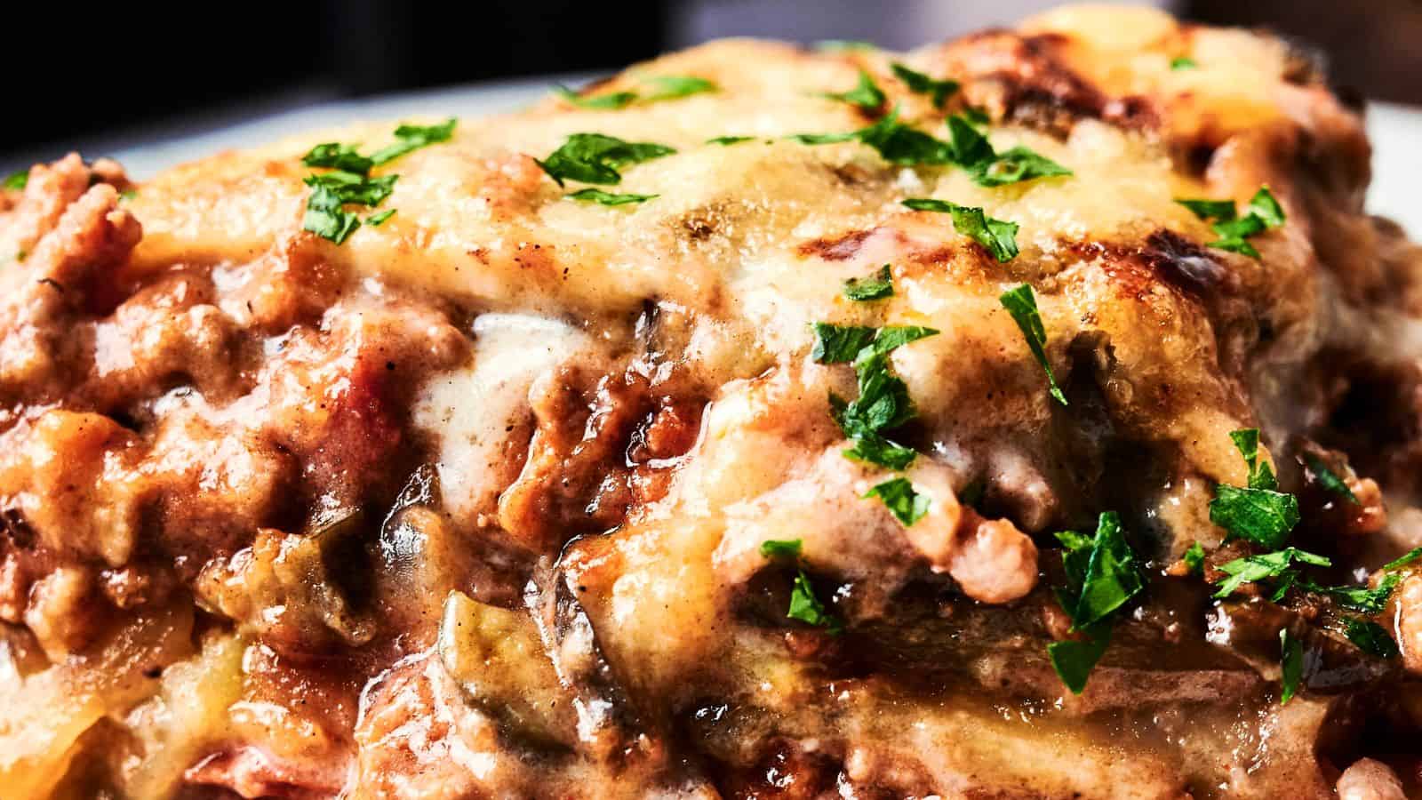 Close-up of a cheesy, baked lasagna topped with chopped parsley and browned, melted cheese.