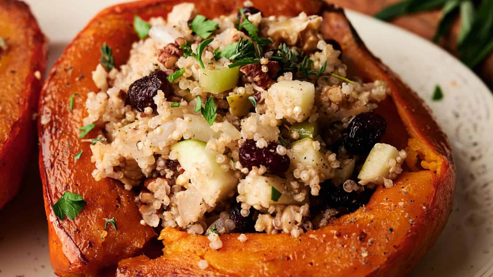 A roasted acorn squash half filled with a stuffing of couscous, apples, nuts, raisins, and fresh herbs sits on a plate.